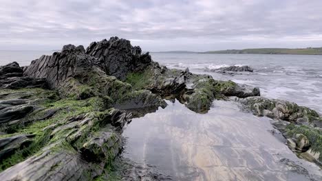 layers of sandstone rocks covered with moss and calm water in shape of a heart with distant waves in slow-motion