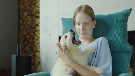 A-teenage-girl-plays-with-a-puppy-of-a-golden-retriever,-sits-in-an-armchair-near-the-fireplace