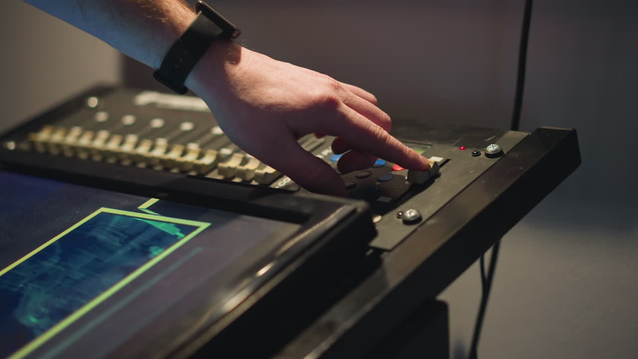 Person adjusting settings on digital lighting control panel, focused on pressing buttons and manipulating dials, controlling lighting for studio production, working with equipment
