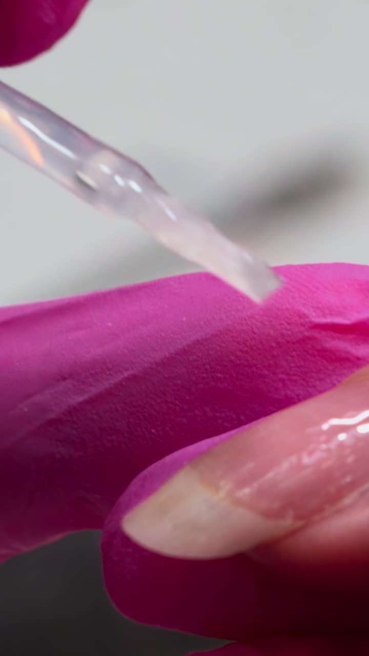 Primer plano de mano aplicando esmalte de gel transparente en una uña