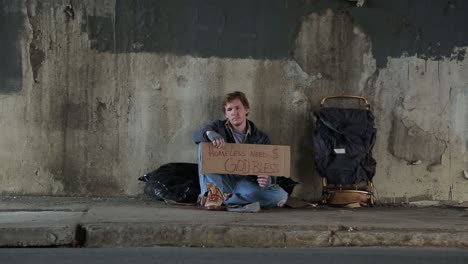 Wide-Shot-of-a-Homeless-Young-Adult-Male-on-the-Street-Holding-a-Sign-Begging-for-Money