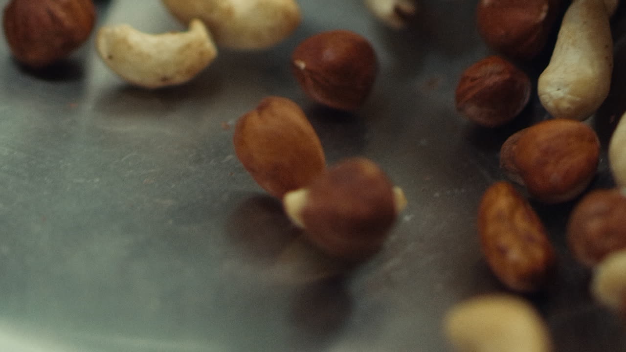 Macro of nuts tossing on pan in slow motion. Closeup cashews and hazel nuts