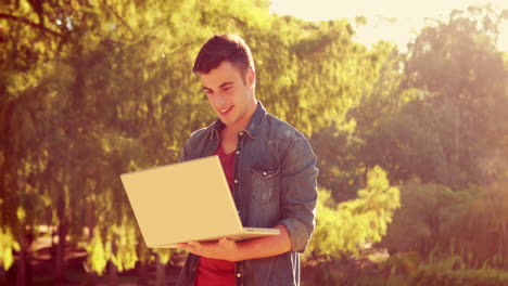 hombre feliz sonriendo a la cámara y usando la computadora portátil en el parque