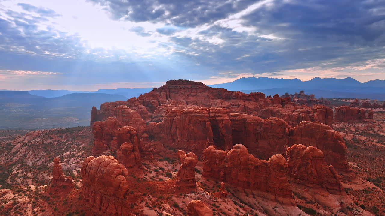 Sunbeams go through the clouds covering the sky. Flying closer to the group of rounded rocks in the Arches National Park in Utah, USA