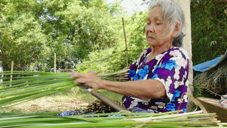 Nahaufnahme-Einer-Frau,-Die-In-Die-Kamera-Blickt-Und-In-Der-Provinz-Quang-Nam,-Vietnam,-Traditionelle-Matratzen-Herstellt.-Die-Materialien-Werden-In-Kleinere-Stücke-Geschnitten-Und-Unter-Der-Sonne-Getrocknet