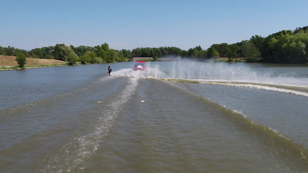 vista aérea siguiendo un barco y un hombre esquiando en el agua - cámara lenta, disparo de drones