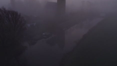 Reveal-shot-of-church-of-Hichtum-Friesland-in-a-foggy-landscape,-aerial