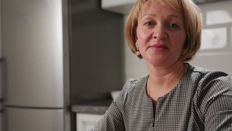 housewife in stripe long gown sits peacefully on kitchen chair resting after cooking, arms folded on countertop near decorated candles, expressing relaxation, and fulfillment after kitchen duties