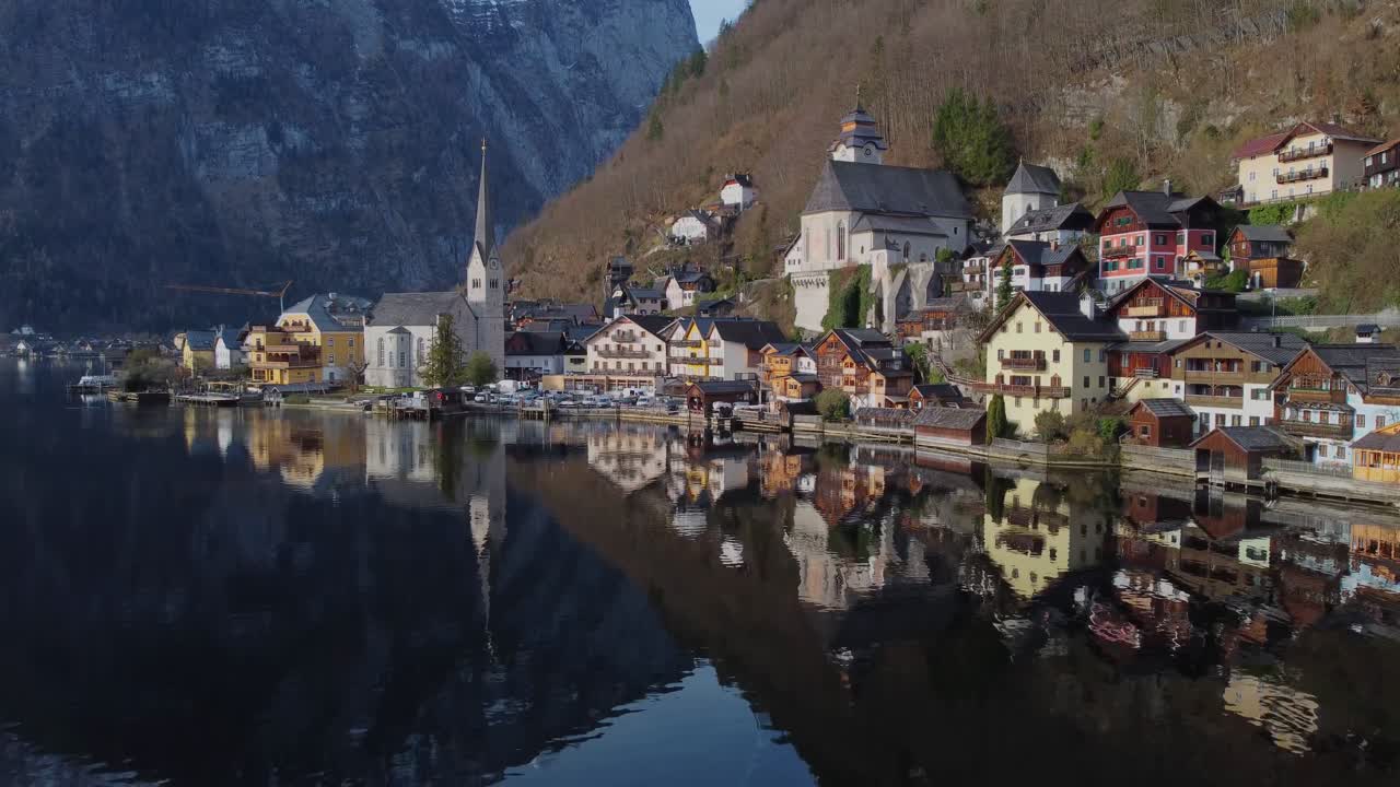 Cinematic drone perspective coming along water towards beautiful lakeside town of Hallstatt on a quiet spring morning - Austria