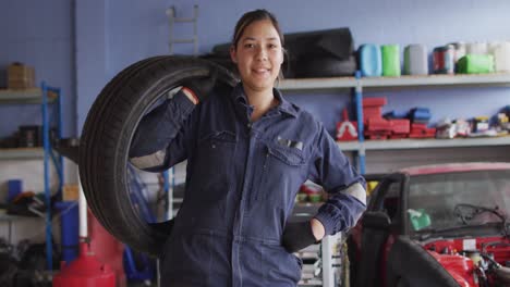 Portrait-of-female-mechanic-holding-a-tire-and-smiling-at-a-car-service-station