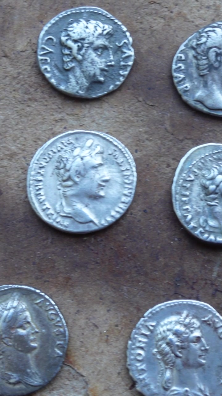 Panoramica su monete d'argento romane di vari imperatori su un antico tavolo di legno. Video verticale