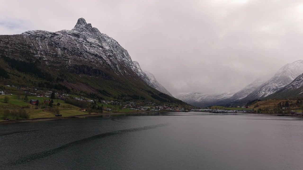 Спокойный пейзаж фьорда в Норвегии с заснеженными горами под пасмурным небом. Идеально подходит для документальных фильмов о путешествиях или сюжетов о природе.