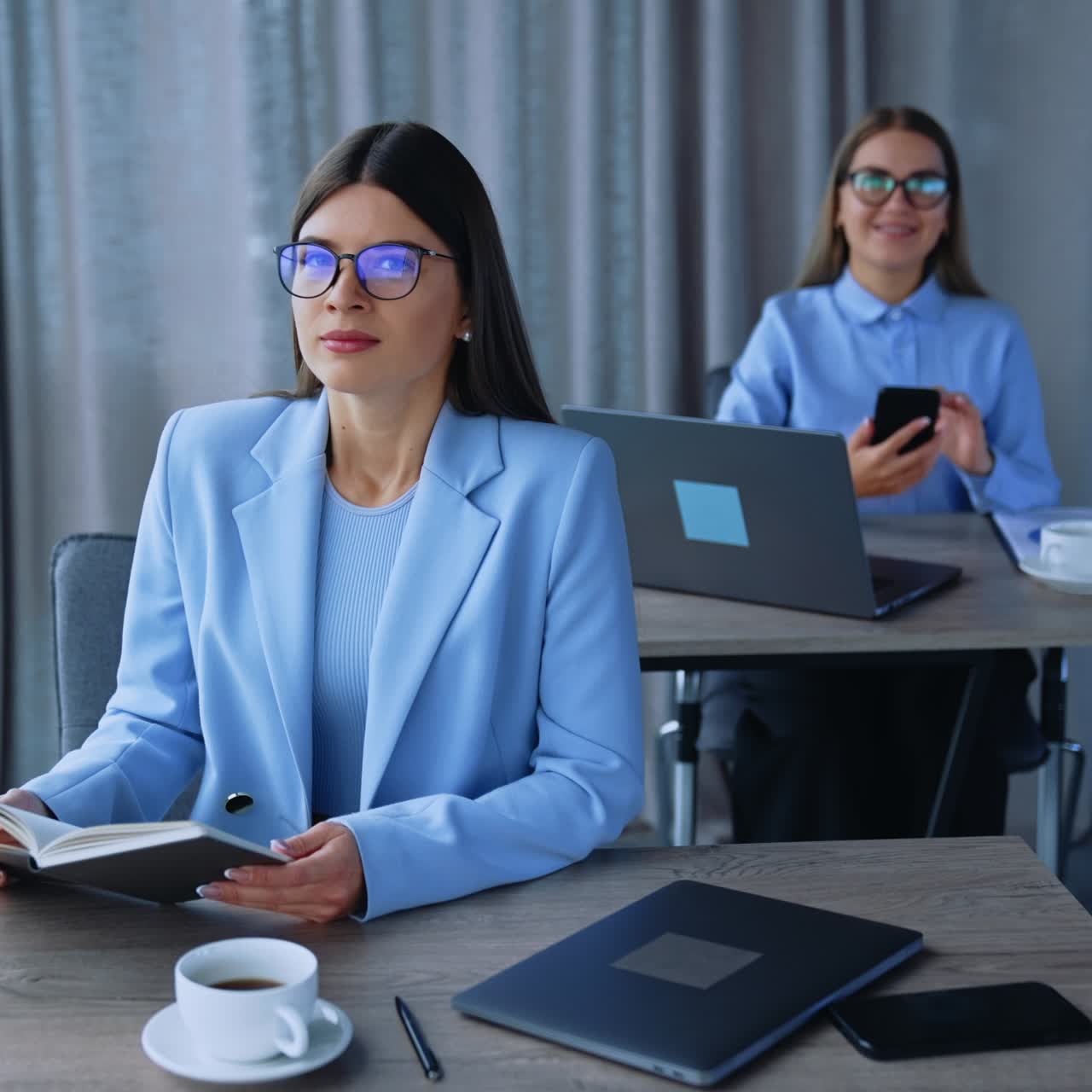 Busy female office employees in the light modern room. Ladies sitting at desks wearing glasses looking into camera