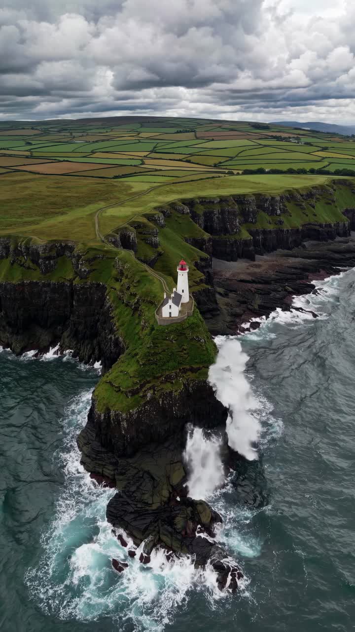 Aerial video captures a dramatic lighthouse perched on rugged cliffs, surrounded by crashing waves