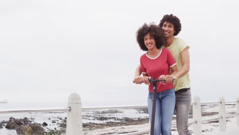 African-american-couple-smiling-while-driving-a-scooter-together-on-the-promenade-near-the-beach