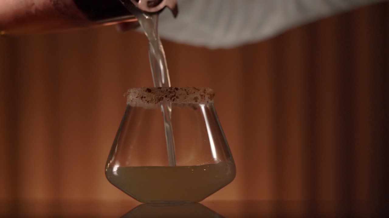 A bartender is pouring a slightly diluted cocktail into a chilled crusted rim cocktail glass.