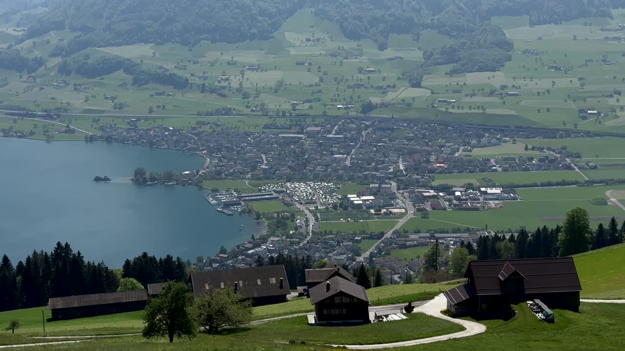 Small swiss city at Vierwaldstättersee during foggy day in summer. Green landscape with huts and farm houses. Aerial top down shot.