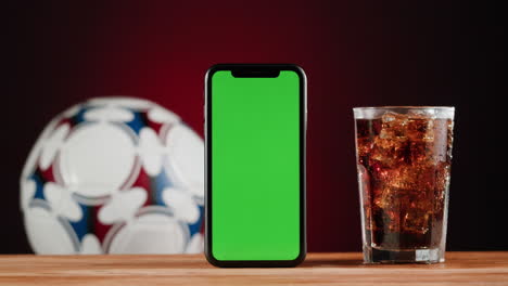 smartphone, soccer ball, and soda on wooden table