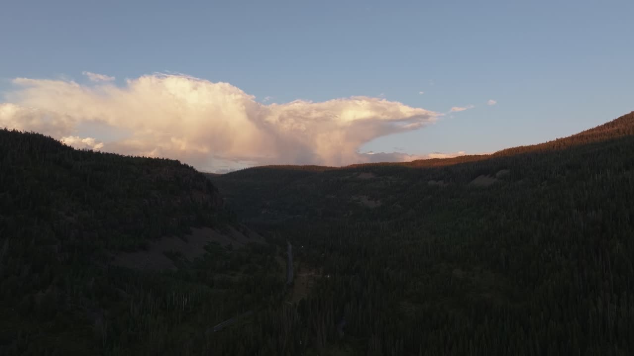 Drone rising wide shot of the Uinta-Wasatch-Cache National Forest in Utah during a summer sunset, pine trees, Provo River, and Bald Mountain and rain clouds rising above the valley