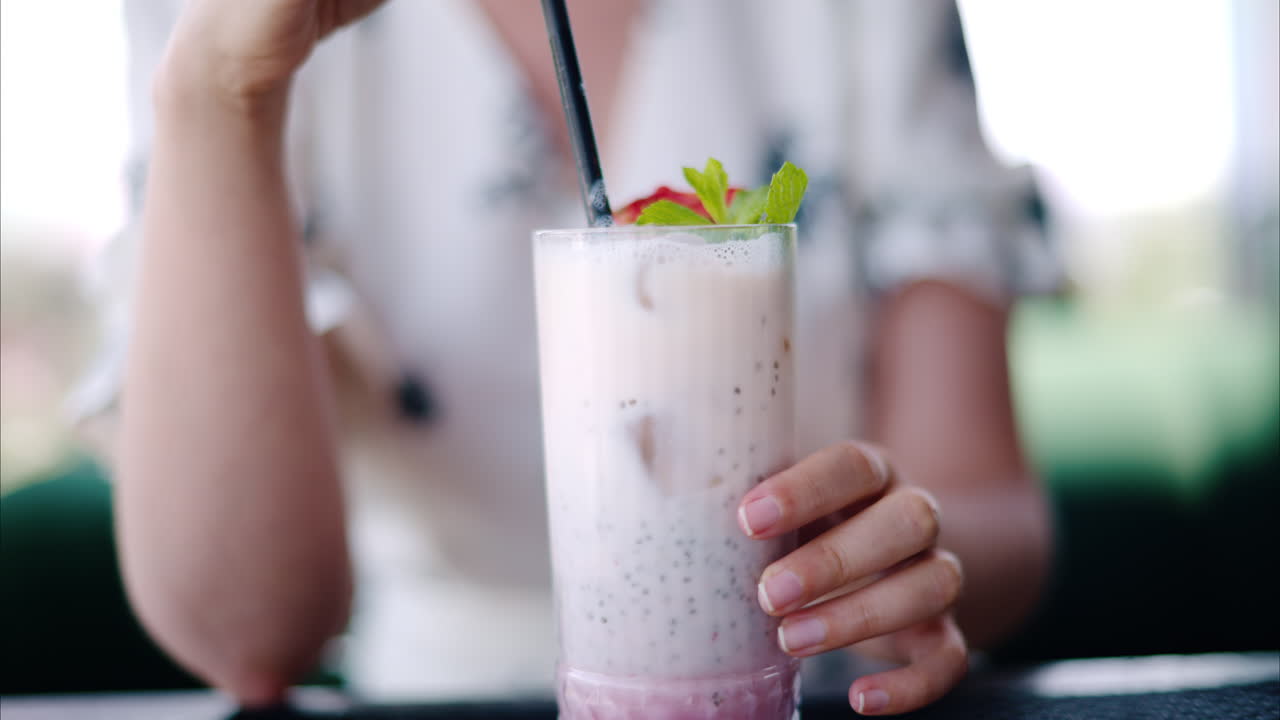 Woman mixing a strawberry drink with a black straw at a restaurant