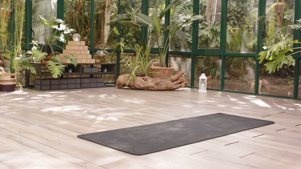 Yoga mat in serene glass house surrounded by lush plants, ready for practice, copy space