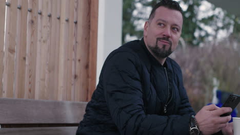 happy middle age man sitting in park and looking at smartphone with smile, slow motion