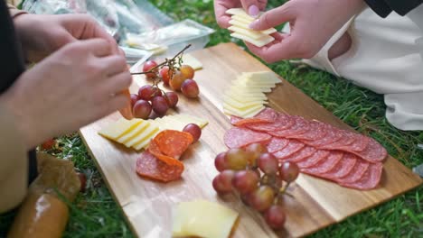 ein paar, das an einem hellen sonnigen tag in einem park auf einem hölzernen schneidbrett ein charcuterie-brett in washington dc herstellt