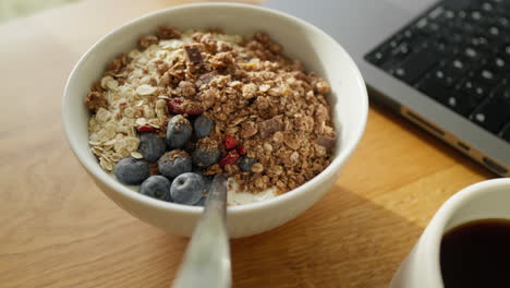 almuerzo con desayuno saludable tazón con granola, arándanos, y un lado de café y portátil