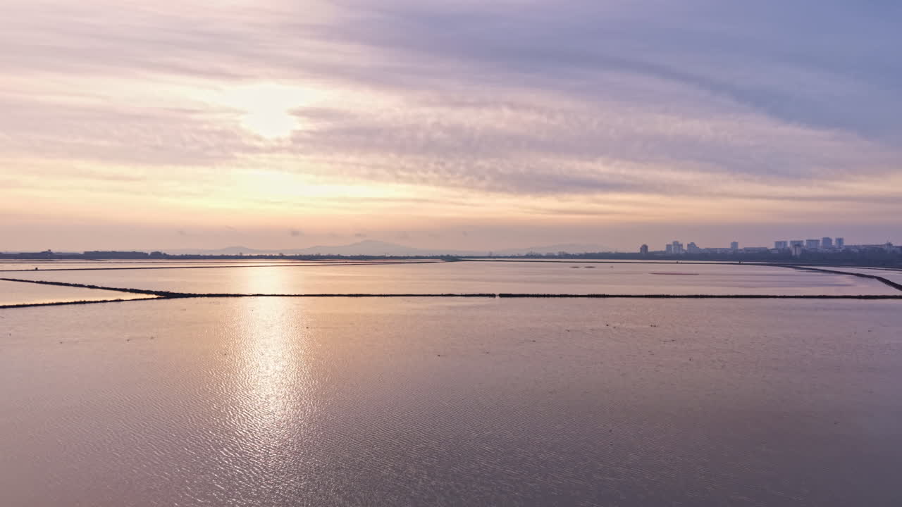 日落时分，金色光芒倒映在沿海城市附近平静的水面上，营造出宁静祥和的景色。
