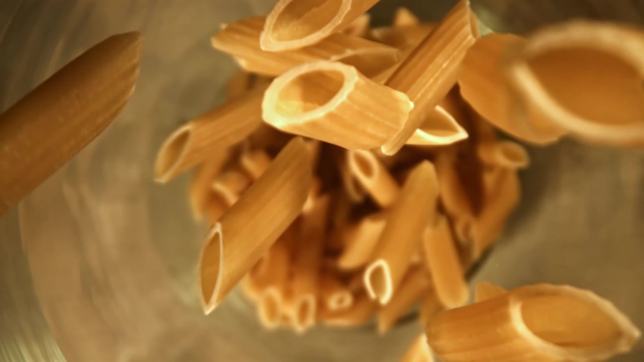 Penne secche che cadono in un contenitore di vetro al rallentatore