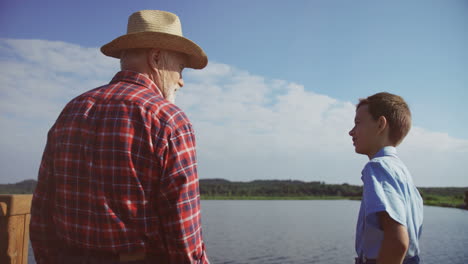 vista trasera de un abuelo y un nieto parados en la orilla de un gran lago o río y hablando