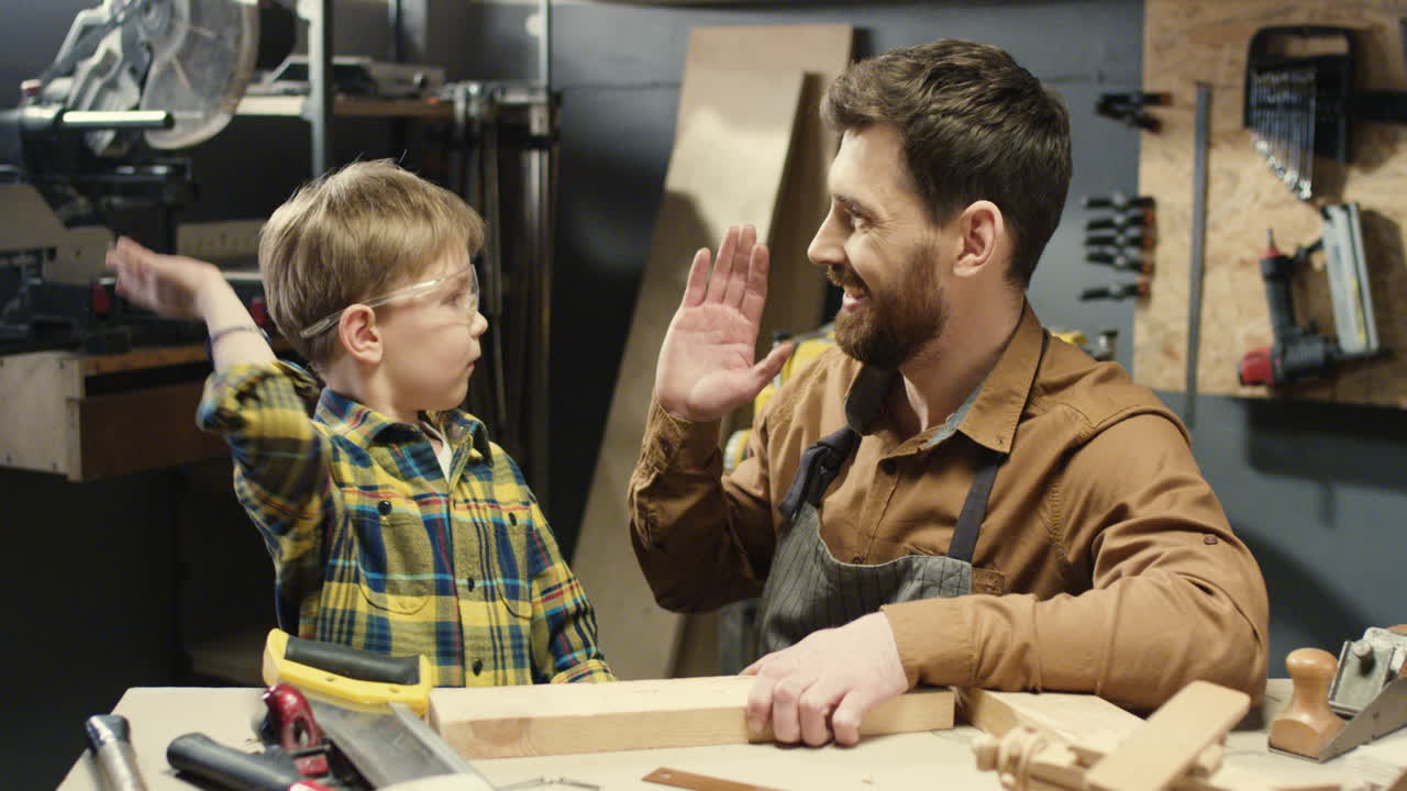어린 아들에게 경재 작업을 가르치고 작업장에서 목재를 톱질하는 백인 목수