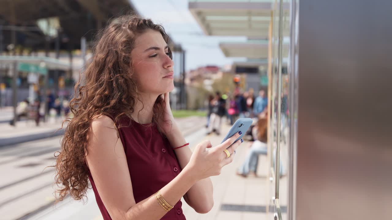 Giovane donna che usa lo smartphone mentre aspetta a una fermata del tram