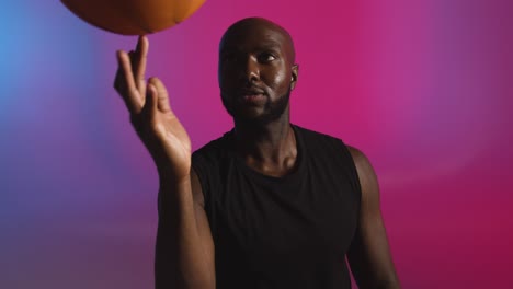 studio portrait shot of male basketball player spinning ball on finger against pink and blue lit background 1