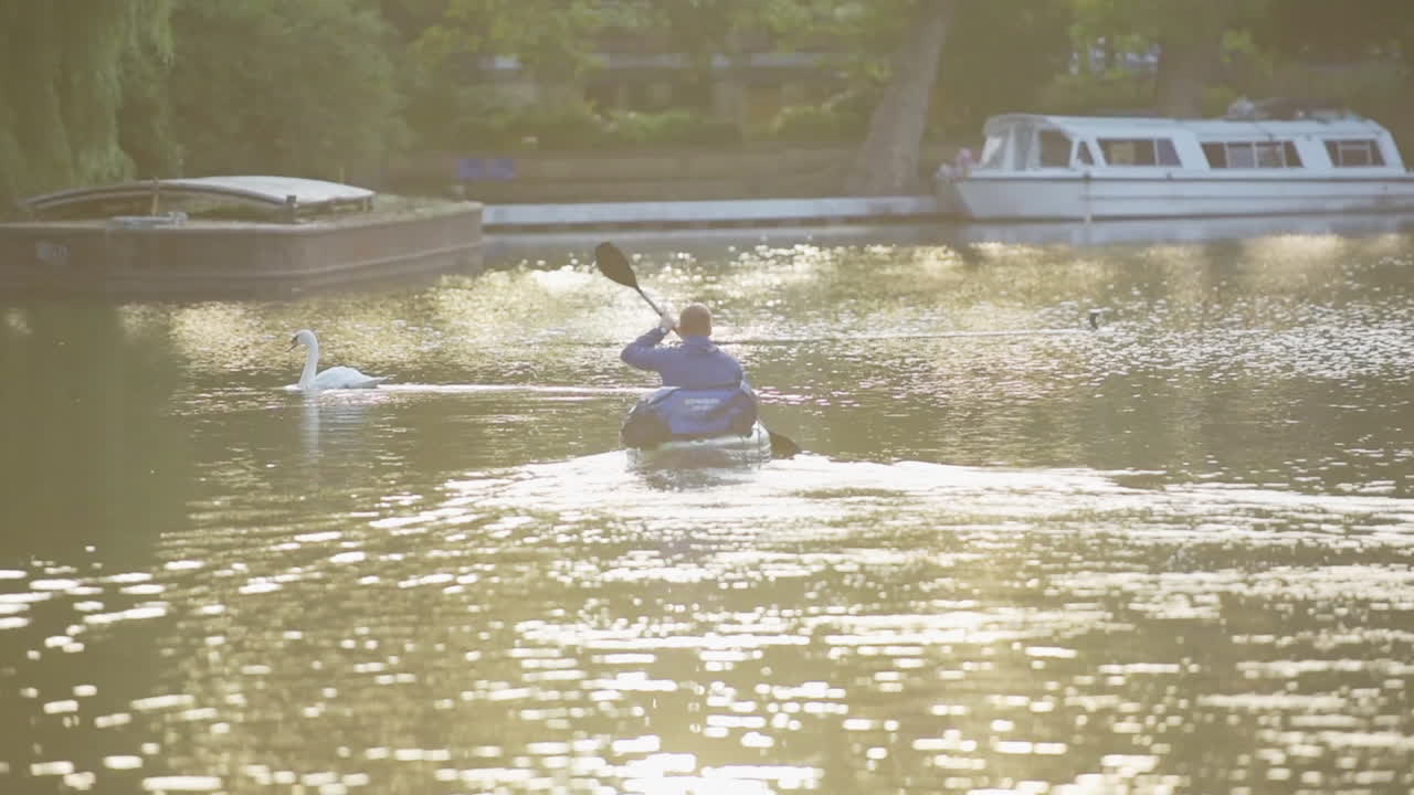 Bright afternoon sunlight shines on an urban kayaker in canals of London, slow motion