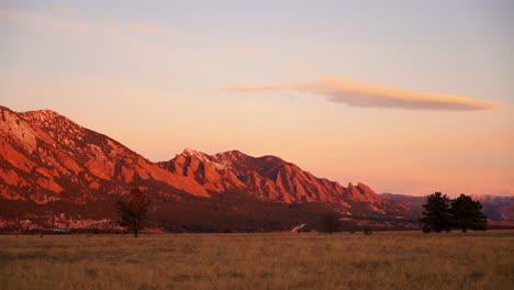 stunning deep orange pink sunrise sunset colorado university boulder flat irons late fall winter dead yellow grass snow on red rocks peaks early morning pan to the left slow motion