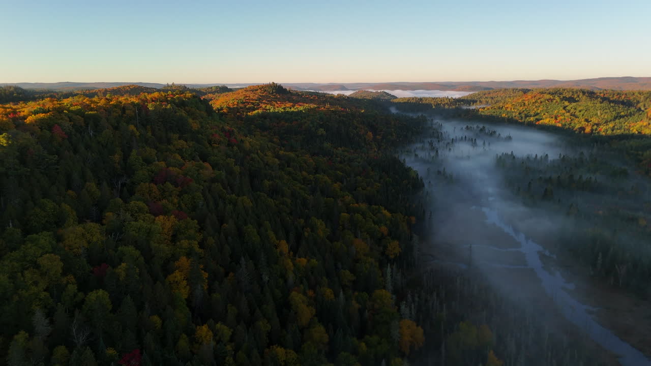 Aerial view of autumn forest and mountains in vivid colors with morning fog in Mauricie, Quebec, Canada. Soft sunlight illuminates the colorful foliage over peaceful wilderness