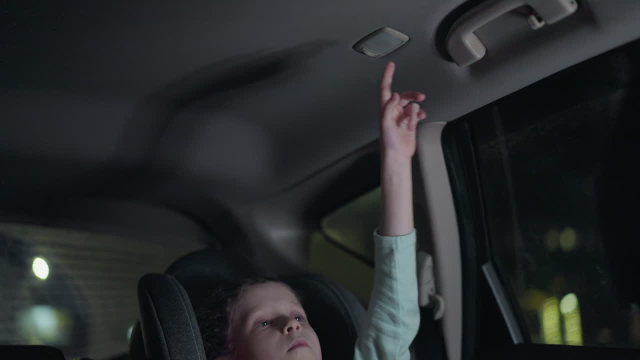 차에서 불을 끄는 아이의 가까운 모습, 배경은 밖에서 흐릿한 불빛으로 희미하게 밝은 차 내부를 보여줍니다.