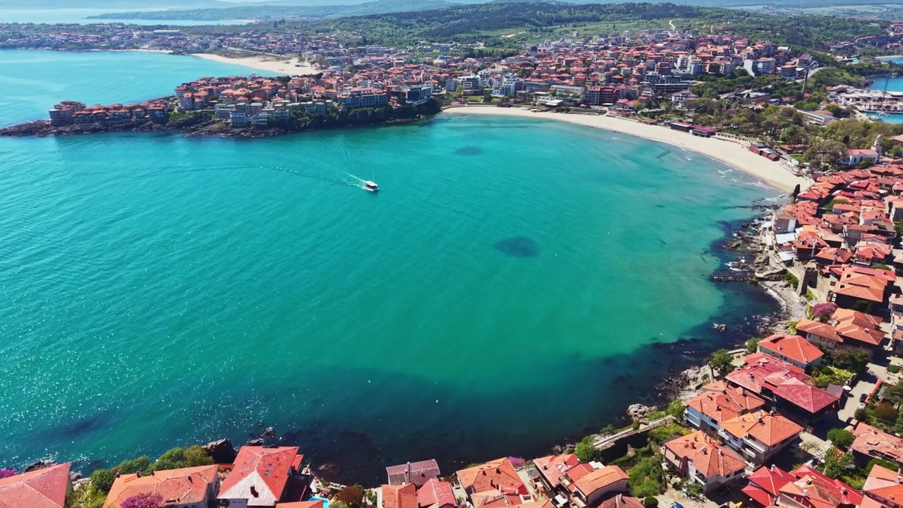 Veduta costiera di una spiaggia assolata con case e acqua azzurra e limpida, vicino a una vivace cittadina nel pomeriggio.