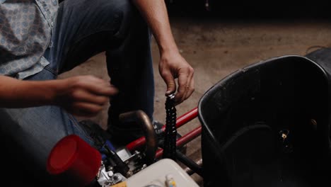 cinematic shot of mechanic re linking the chain of his diy go kart with tongs