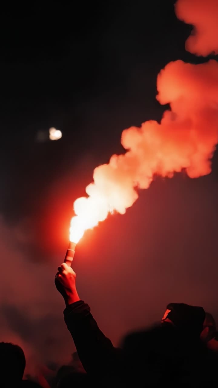 A Hand Holding a Red Flare Illuminates the Night, Casting an Eye-Catching Glow Over a Crowd, Symbolizing Passion and Energy in a Nighttime Display