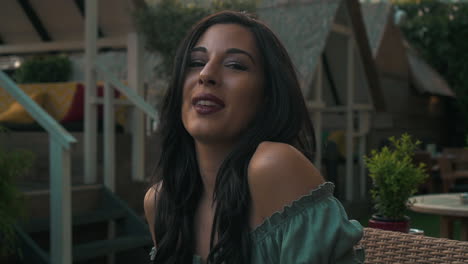 Slow-Motion-portrait-of-a-beautiful-hispanic-latino-young-woman-looking-at-the-camera-and-show-emotions-from-serious-to-smiling-and-laughing-while-seated-in-a-club-at-sunset