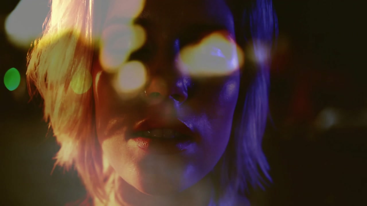 Camera rising revealing teenage performer lip syncing chain glinting under bokeh lights for music