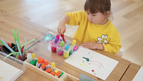 child girl study dropper painting sitting by the desk, sucks in colored water into pipette from containers - high angle