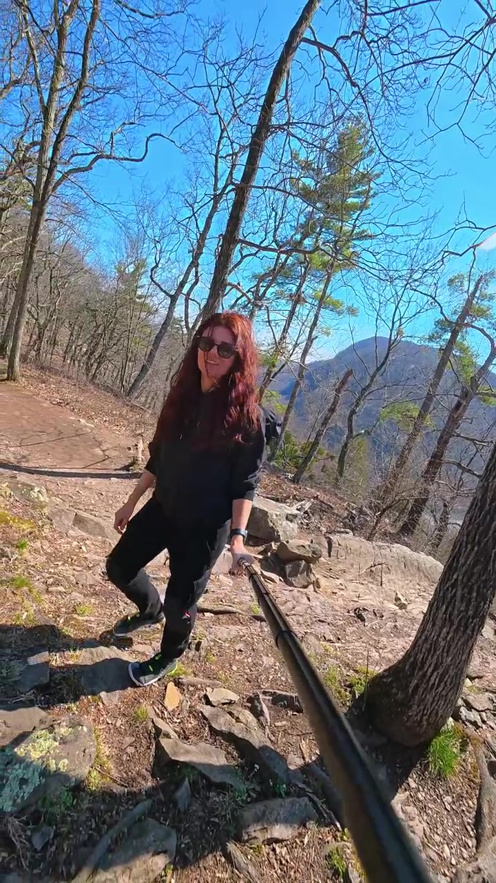 Escursionista donna che cammina su un sentiero roccioso in cresta sul Monte Tammany. Una donna con uno zaino cammina lungo un sentiero roccioso a strapiombo accanto a un tronco d'albero, con vista sulla valle del Monte Tammany.