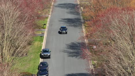 Black-sedan-drives-along-calm-empty-road-lined-with-leaveless-trees