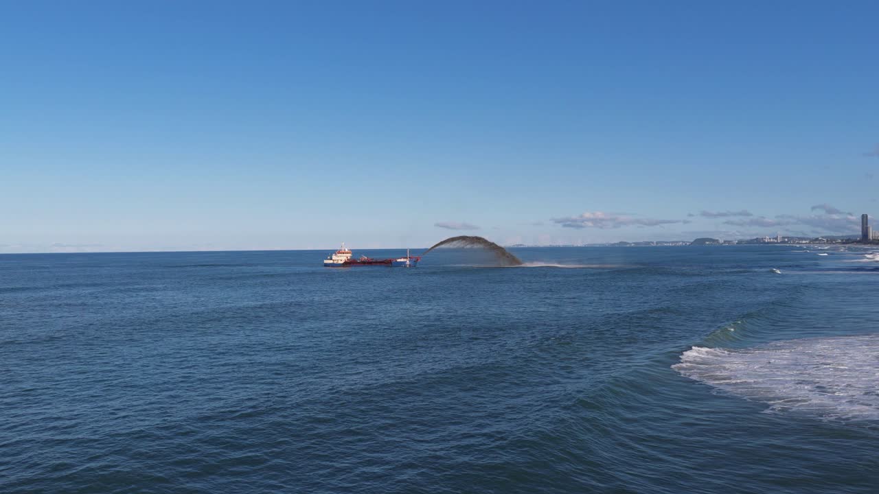 A dredging ship pumps sand to restore beach erosion at Surfers Paradise, Gold Coast. Clear skies and calm seas enhance the scene