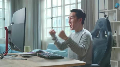 Asian Man In Long Sleeved T-Shirt Looking At Desktop Computer Screen And Being Happy After Winning The Project While Working At Home.
