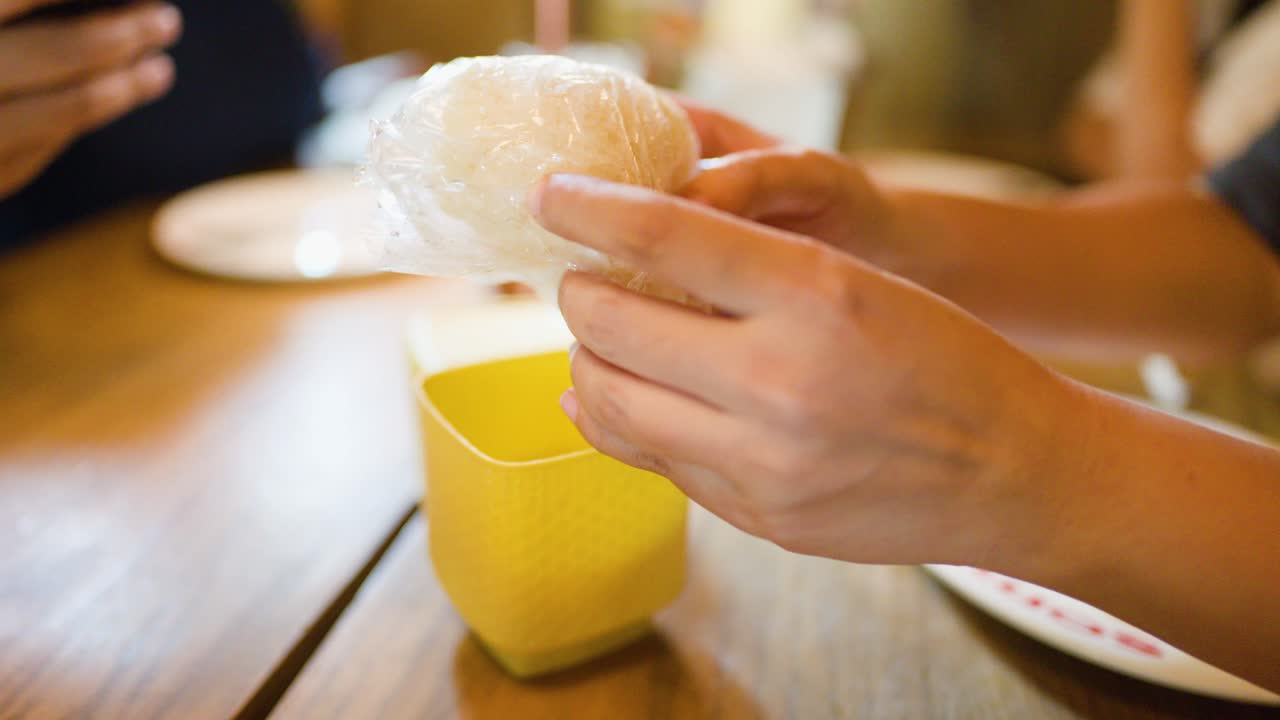 Hands remove sticky rice from yellow wicker basket in bright, casual Thai restaurant setting