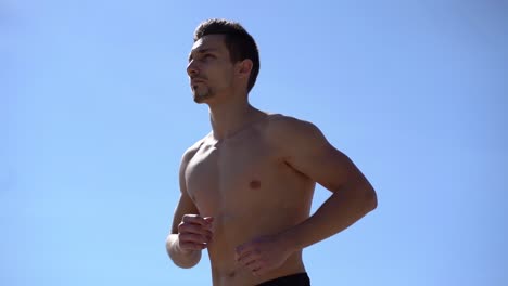 muscular shirtless man running against blue sky